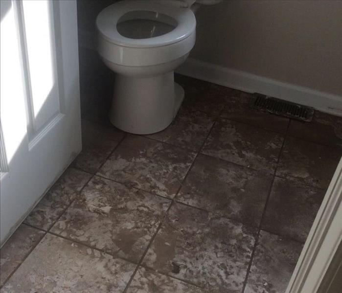White and tan bathroom and toilet with dirty water on the floor