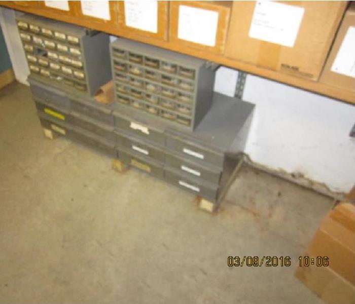 Warehouse metal shelving under wood shelving in front of a white wall