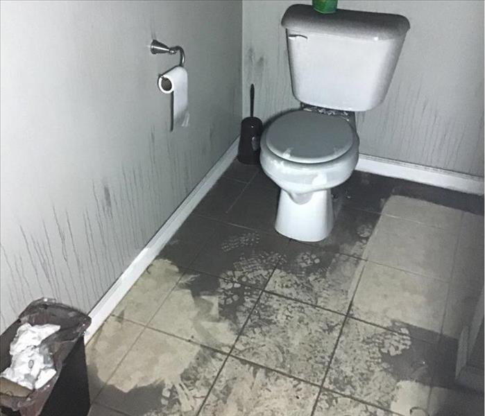 black soot and ash in bathroom with white tile, toilet and gray walls